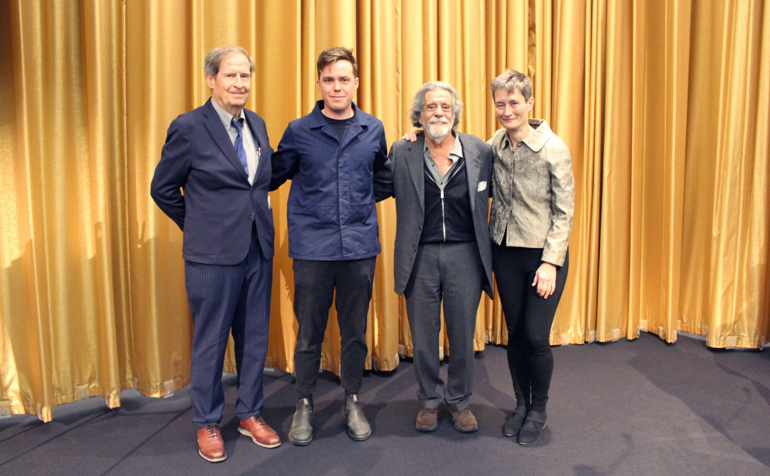 Four people standing with gold curtain in background