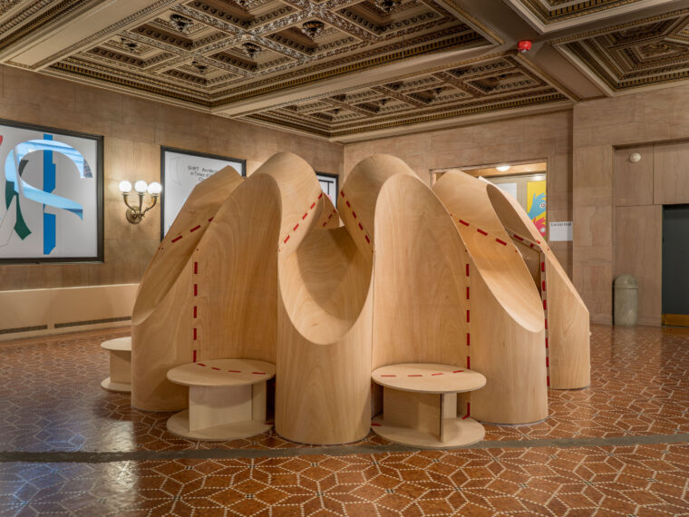 Large sculptural seating installation made of smooth, pale wood panels.