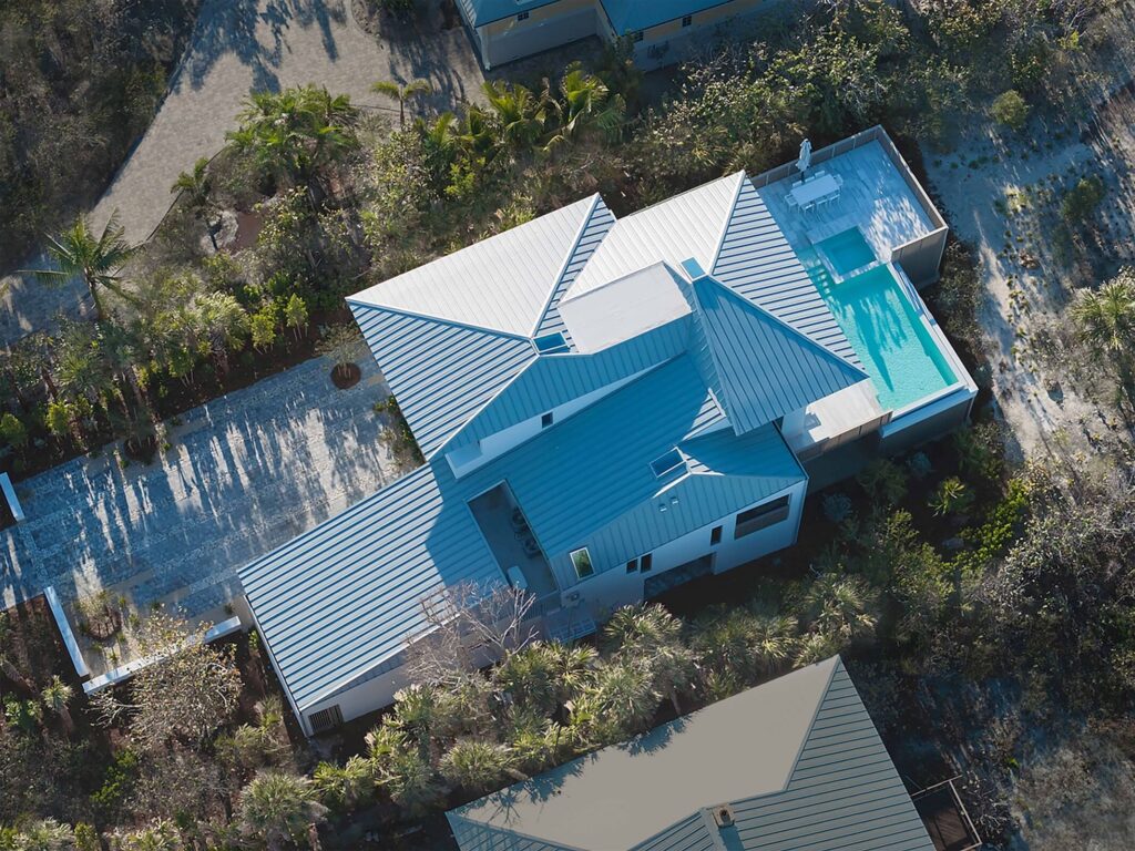 Aerial view of a modern white house with multiple metal roofs and a rectangular pool.