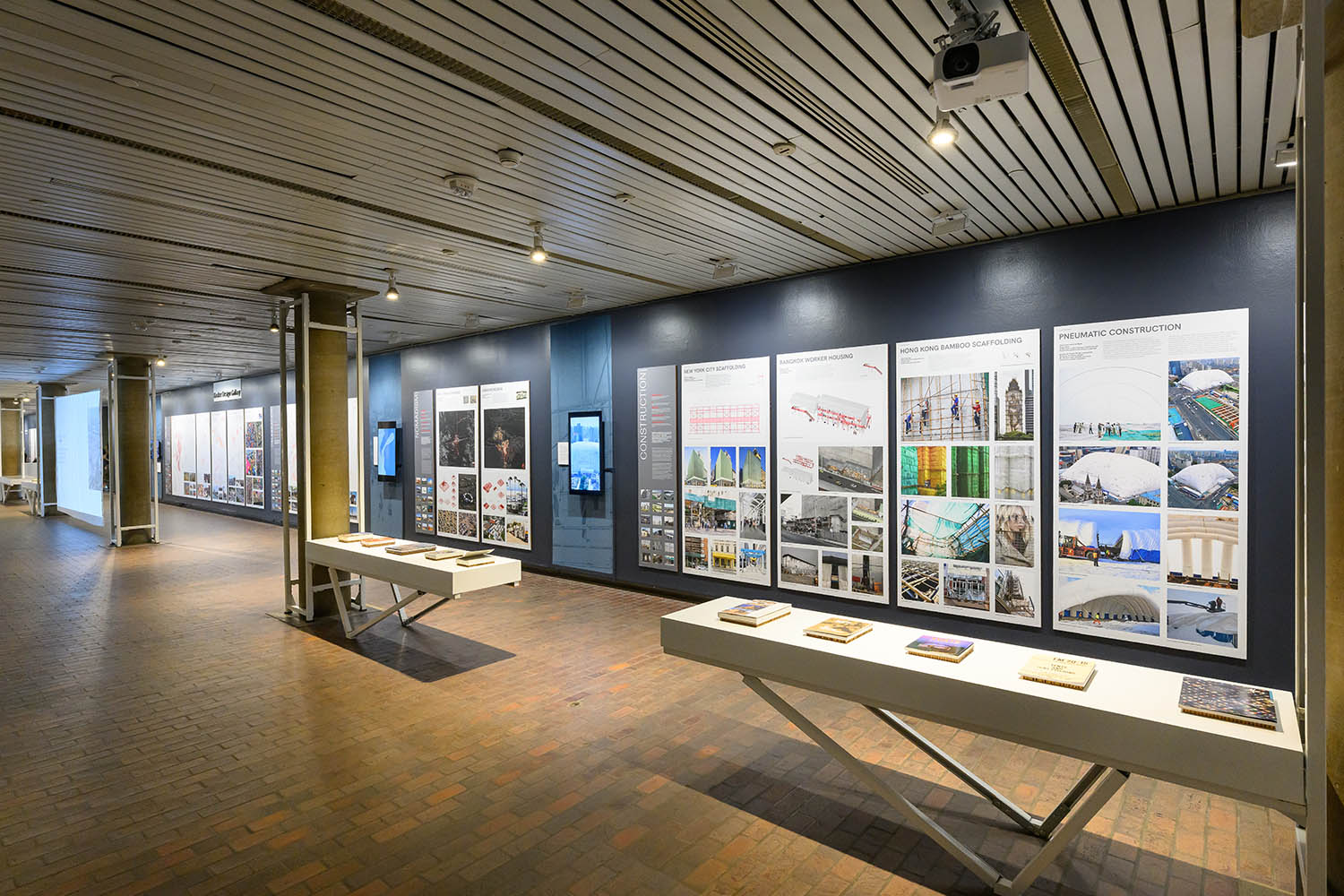 A long wall displaying a row of panels depicting maps and photos. Two long shelves of books are in front.