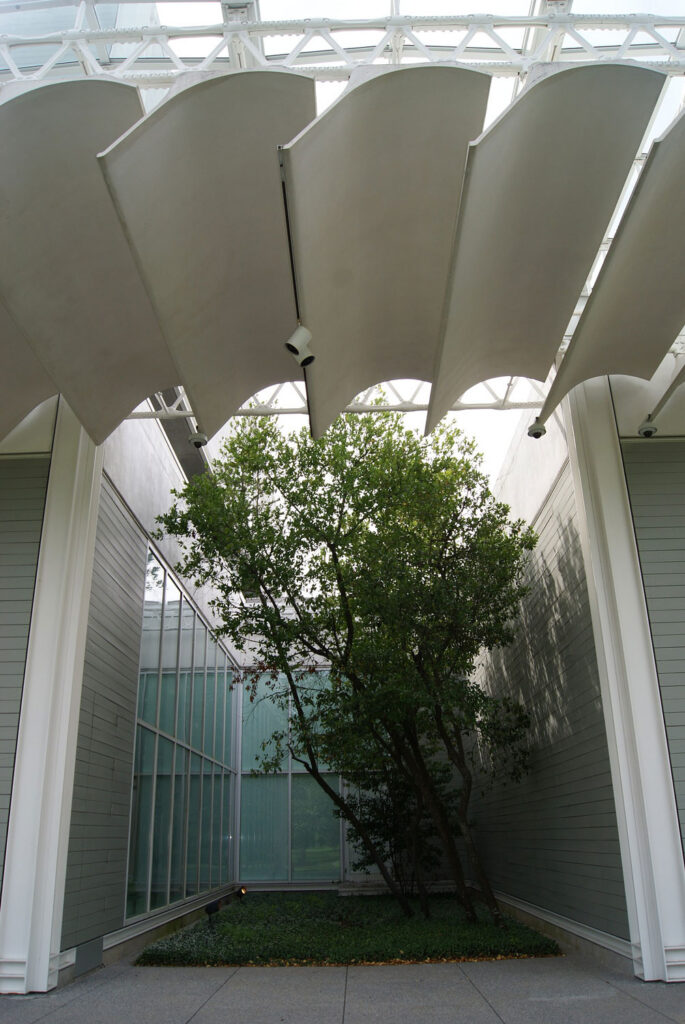White shading louvers in a white frame around greenery.