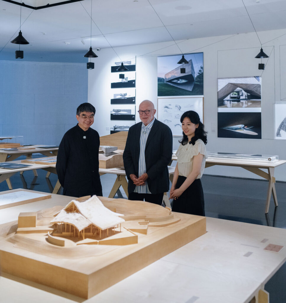 Three people in a room with drawings and models.