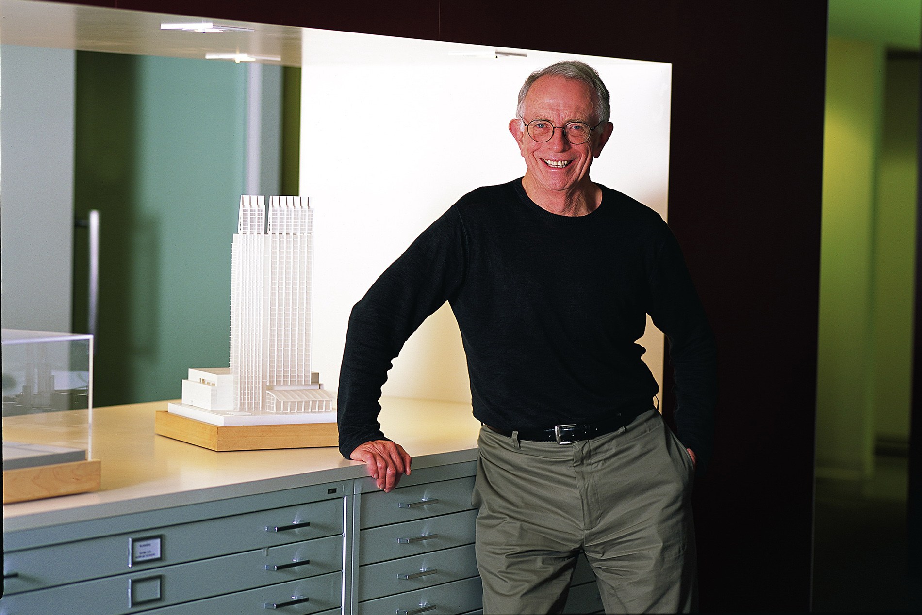 Bill Valentine stands in front of an architectural model smiling