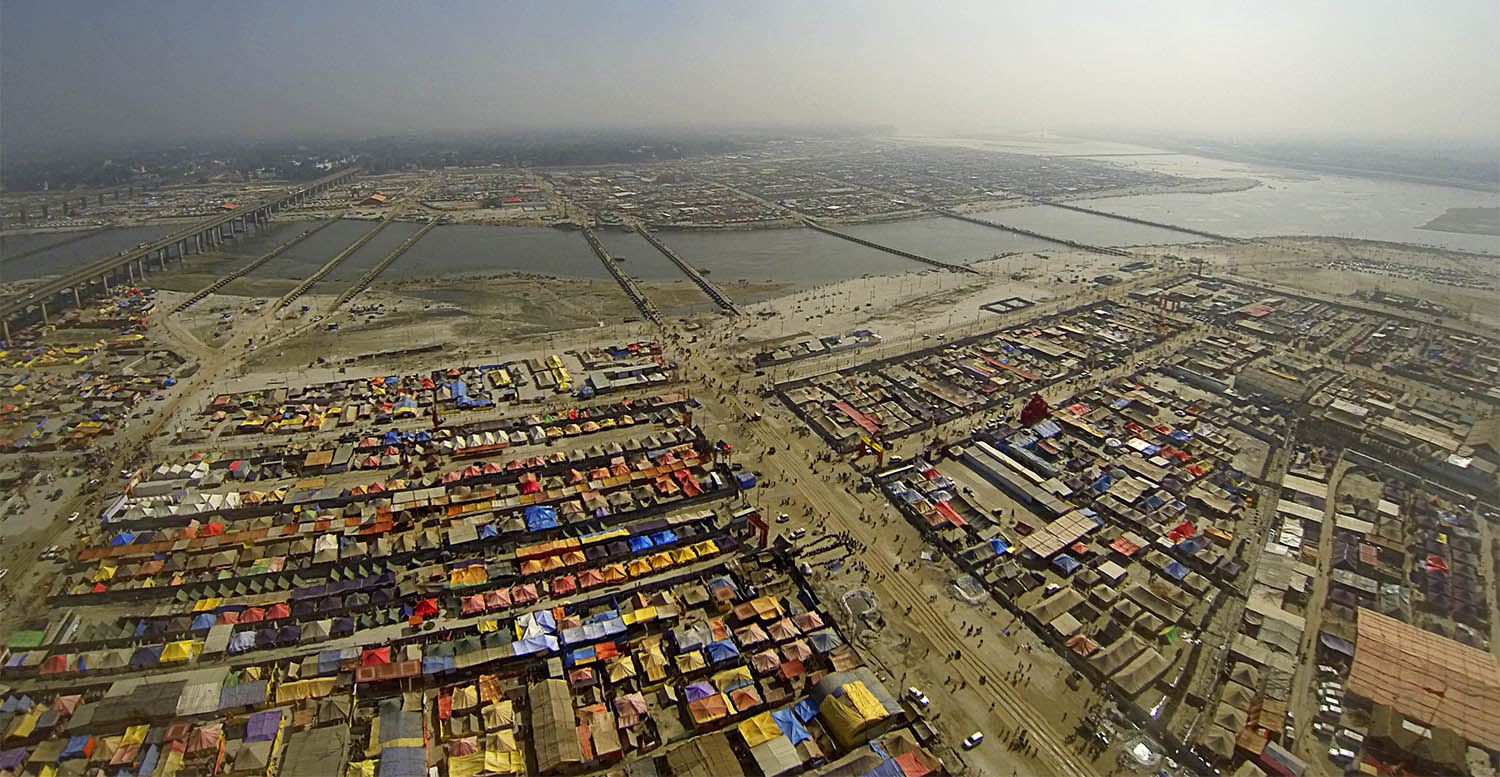 Aerial view of a vast colorful temporary city with people. and vehichles moving down a main ,dirt road.