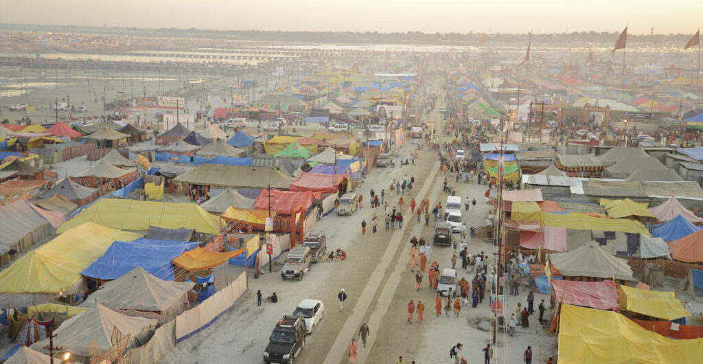 Aerial view of a vast colorful temporary city with people. and vehichles moving down a main ,dirt road.
