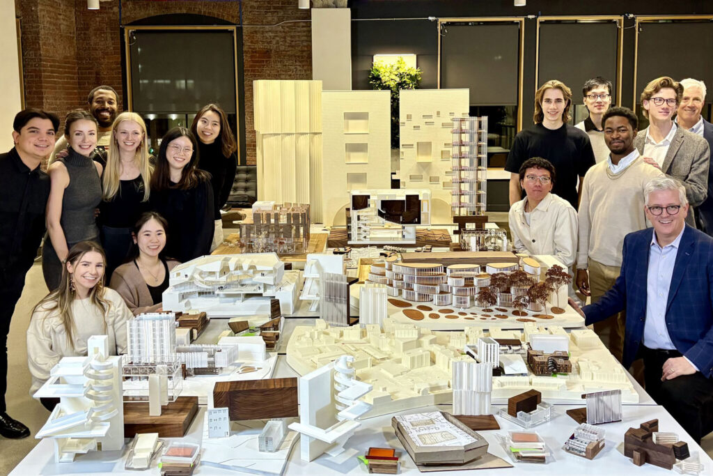 A dozen people with building models in an office smiling.