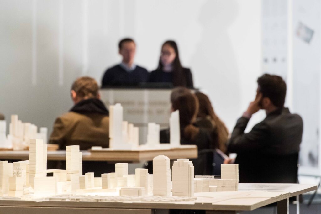 Photo of architectural models with students and presenter in background.