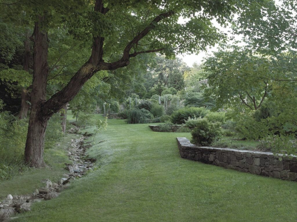 winding cobblestone drainage on the left and a low curved wall on the right in a green garden