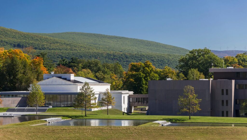 A white domed building beside a reflective pool, with a low green mountain behind.