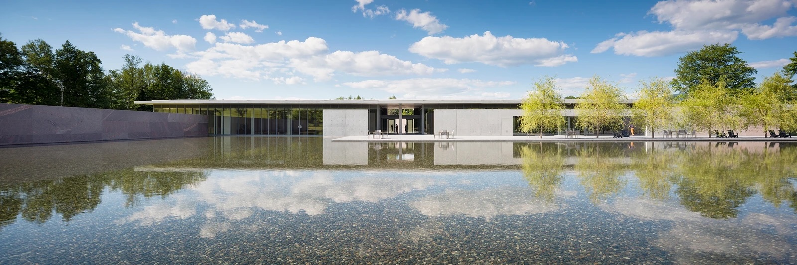 a reflective pool on a sunny day holds white clouds, outside a low modernist building
