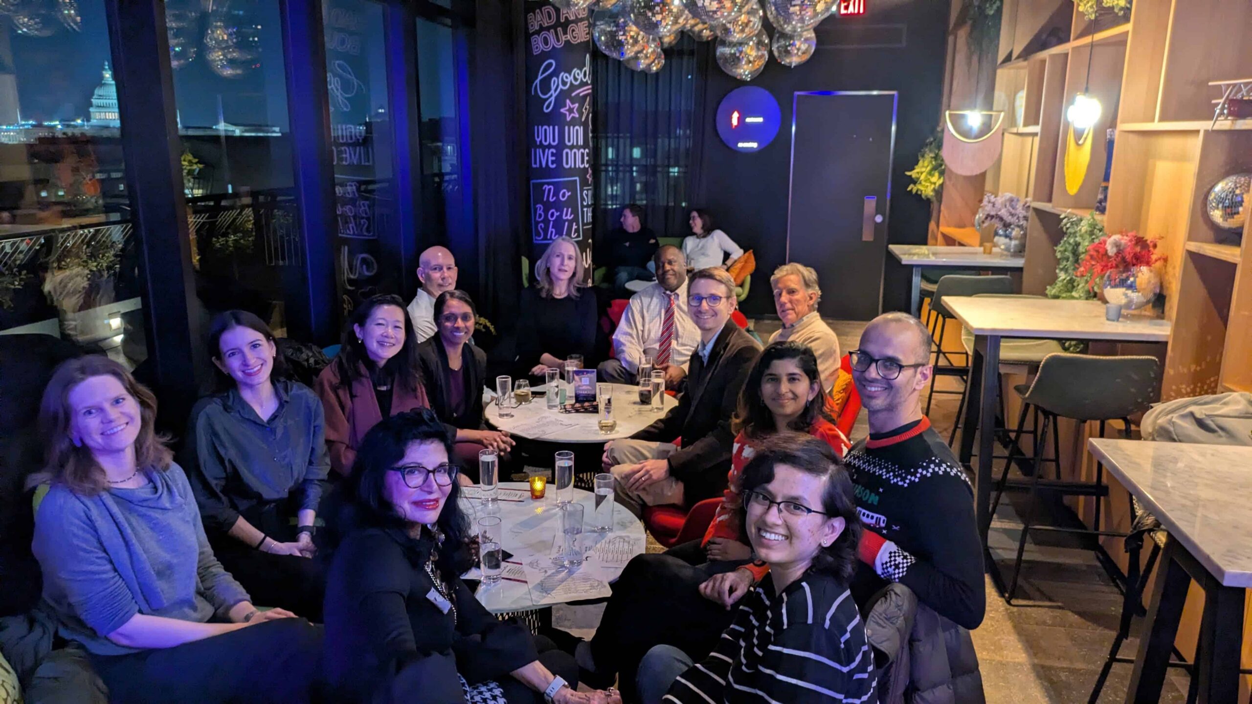Group of people seated around a restaurant table beneath blue lighting.