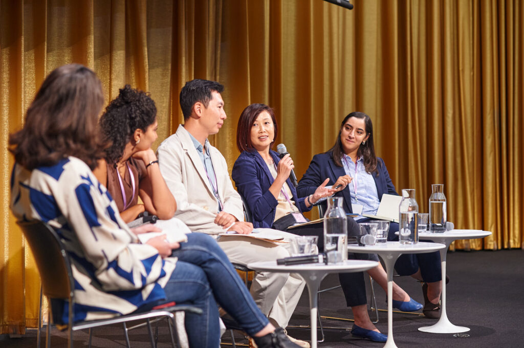 A panel of five people in Piper Auditorum. A woman in the center holds a microphone.