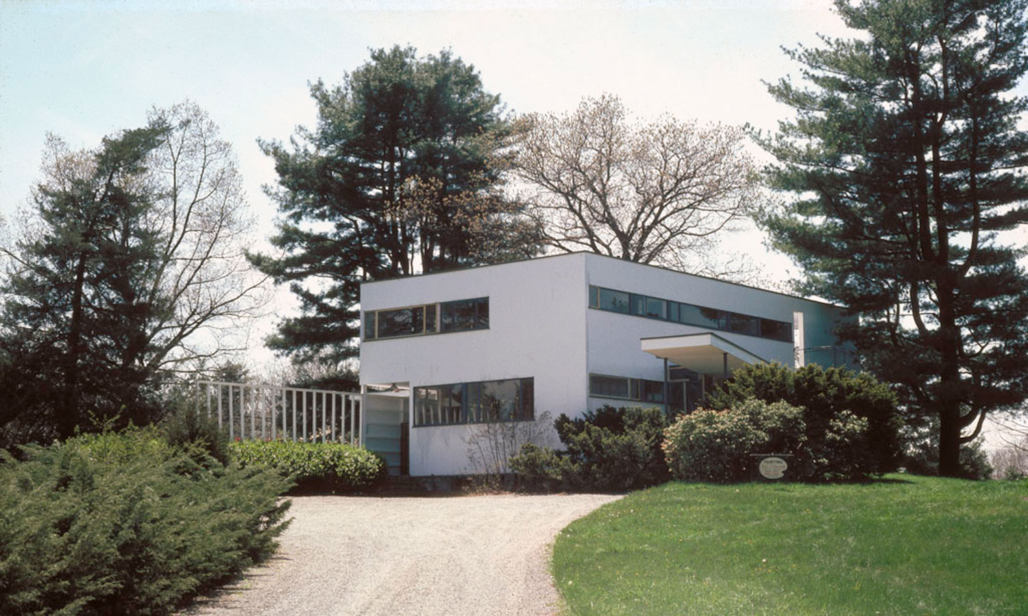 White angular house amid trees with access lane.