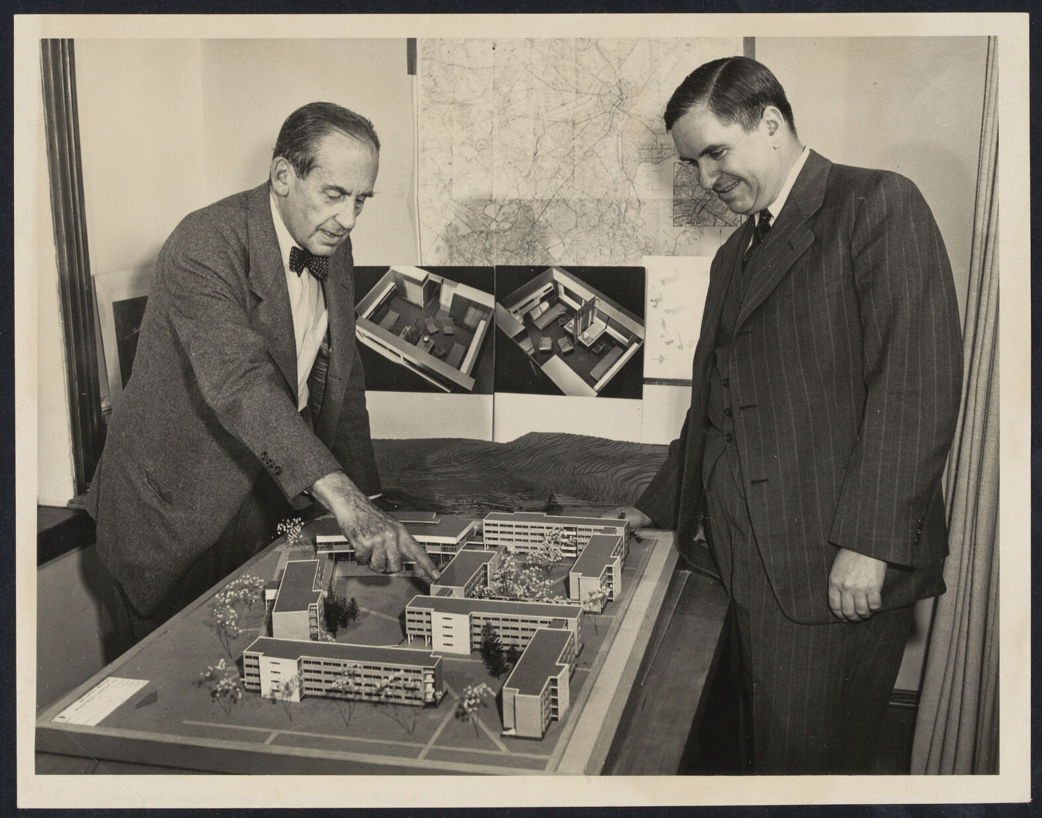 Two men look at an architectural model of a large building complex.