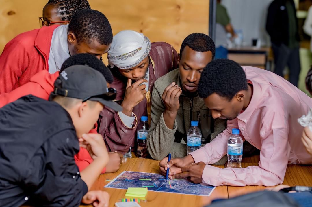 A group of people leans over a printed map on a table, discussing it and marking locations with colored pens and sticky notes.
