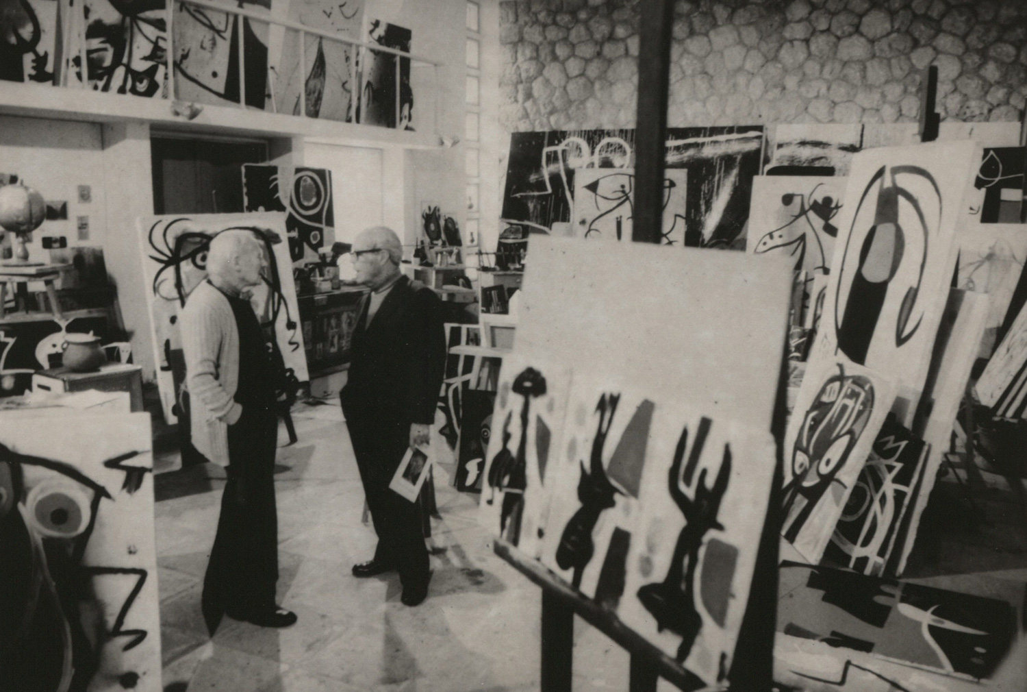 Two men in a studio filled with artworks.