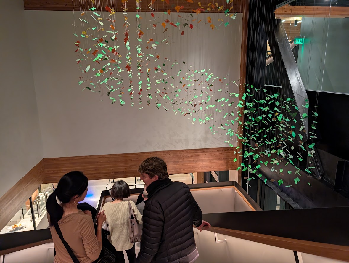 Several people walking down a modern staircase beneath a suspended installation of colorful leaf-shaped pieces.