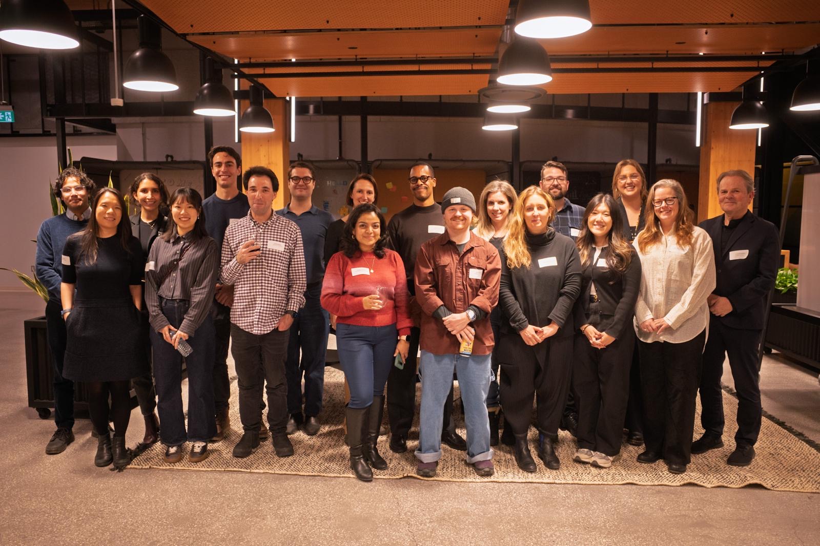 Group portrait of about 20 people standing together in a warmly lit modern office or event space.
