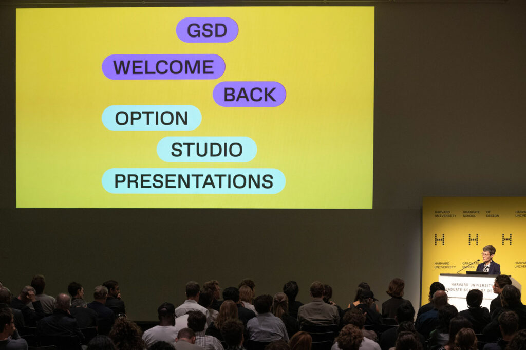 Sarah Whiting speaks at a podium in Piper Auditorium while a screen displays the text GSD Welcome Back Option Studio Presentations.