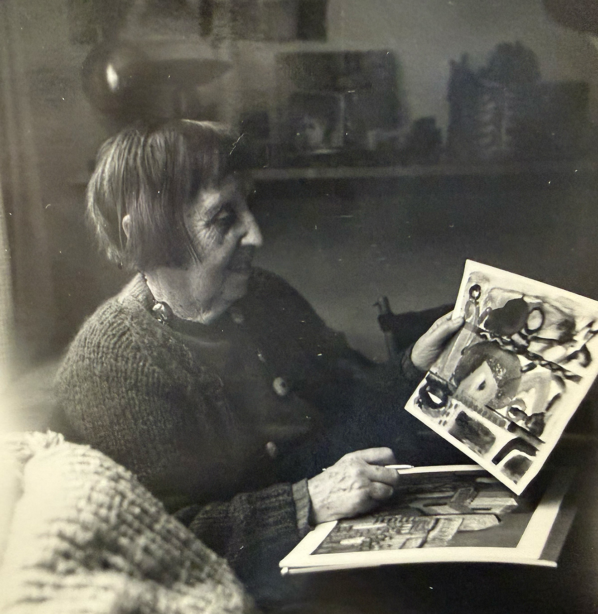 A woman sits in profile holding up an abstract painting or textile.