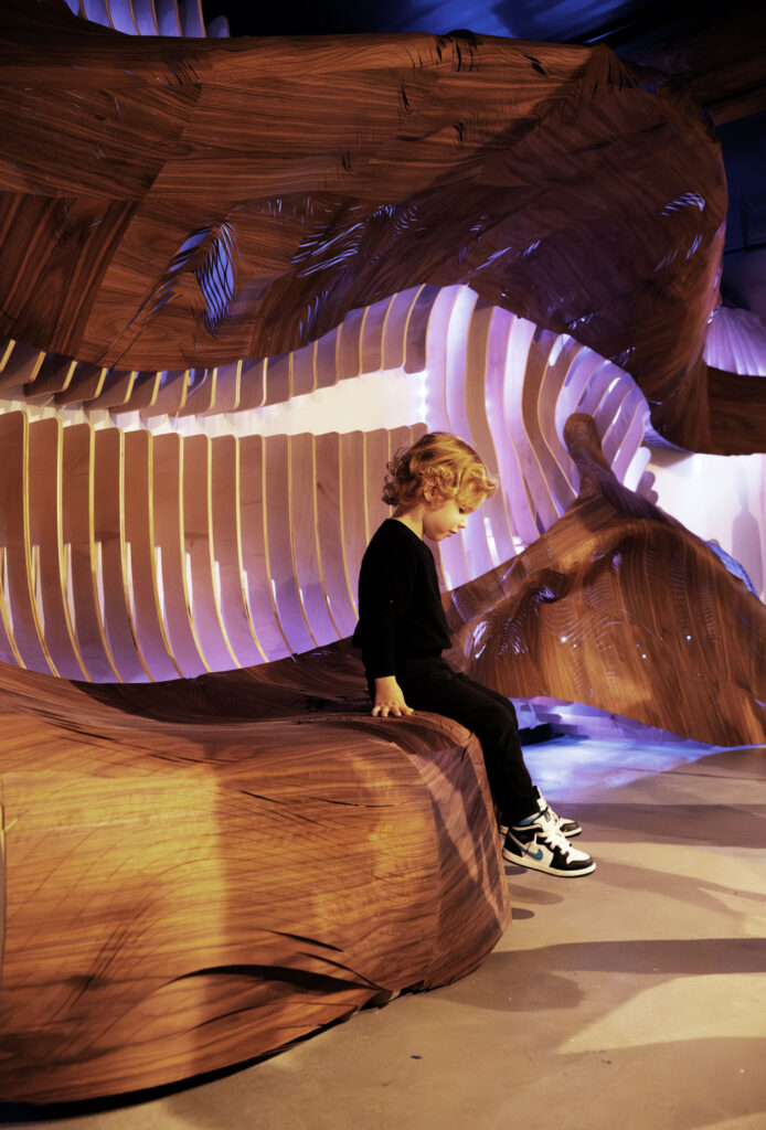 A view of the installation Animated Materiality with a child sitting on a wooden ledge.