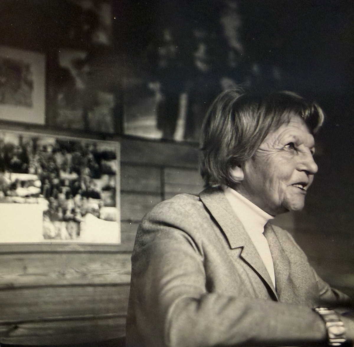 A woman on the right side of the frame, in a light blazer and white shirt, looks to the right.